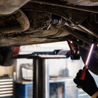 A mechanic inspecting the underside of a car with an inspection light