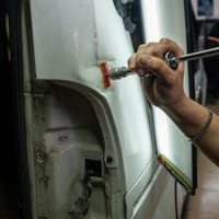 A hand using a tool on a car body panel