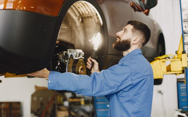 A mechanic inspecting a brake caliper with a work light
