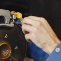 A hand working on a brake caliper with a tool