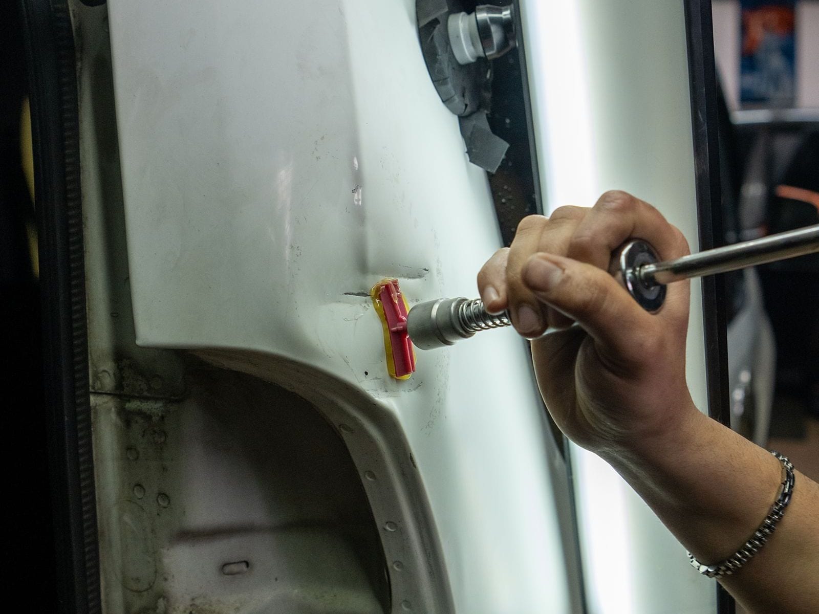 A paintless dent repair tool pulling a dent from a car door