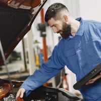 A mechanic holding a diagnostic scan tool at an open car hood