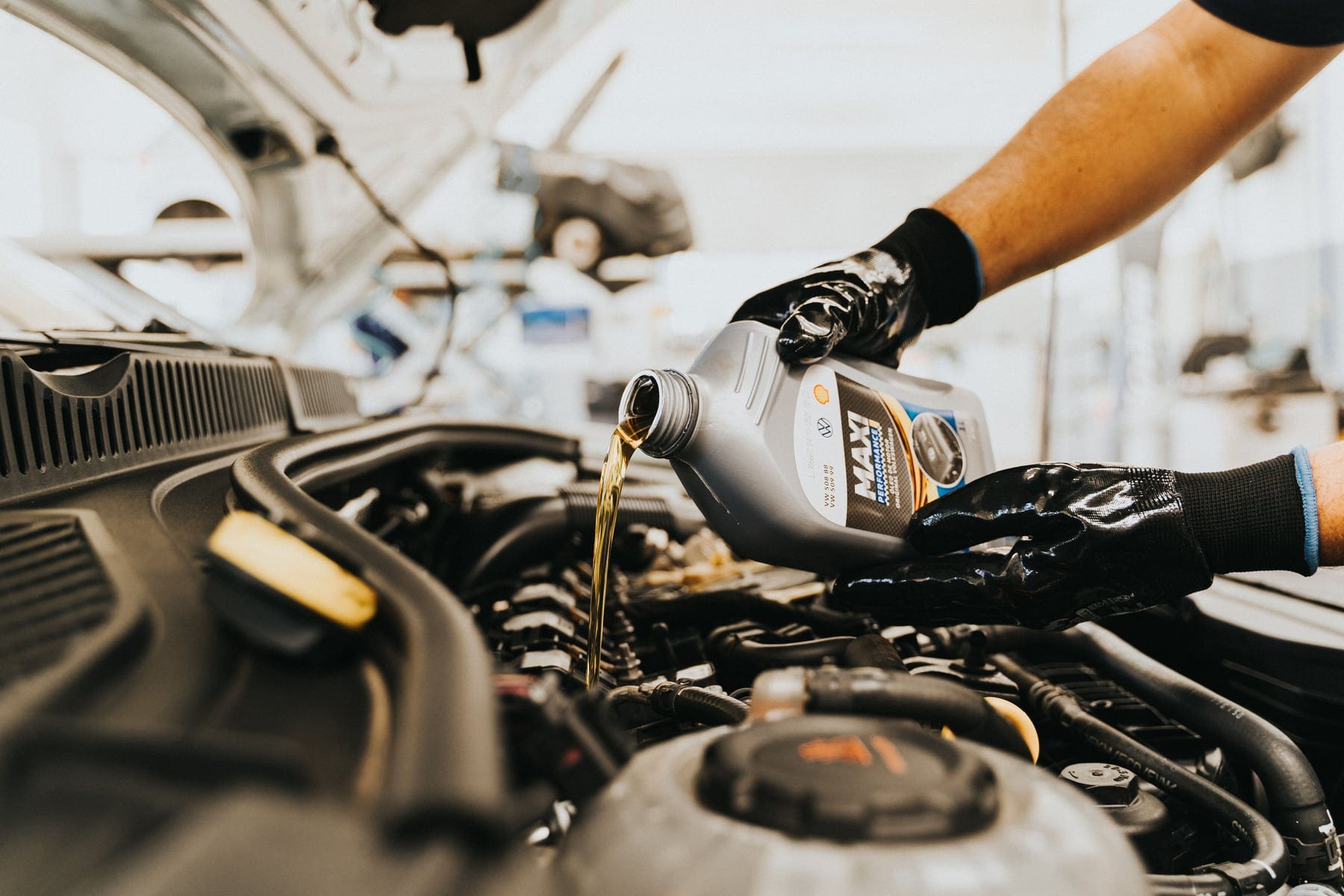 Gloved hands pouring motor oil into a vehicle engine