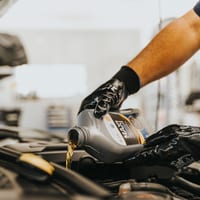 Gloved hands pouring fresh motor oil into an engine