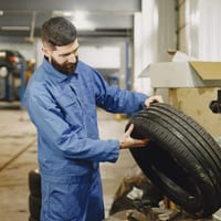 A mechanic holding a tire beside shop equipment